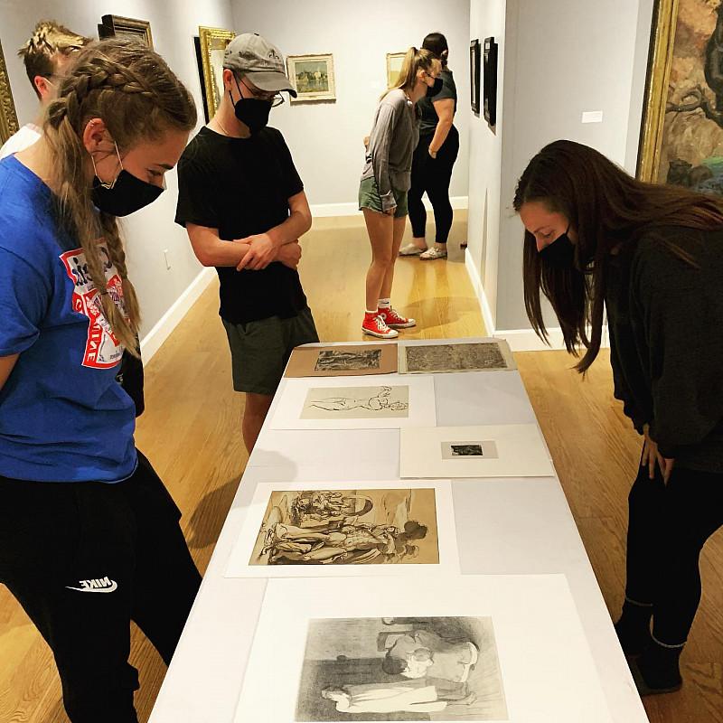 学生们站在赖特艺术博物馆的画廊里，看着桌子上和墙上的艺术作品.